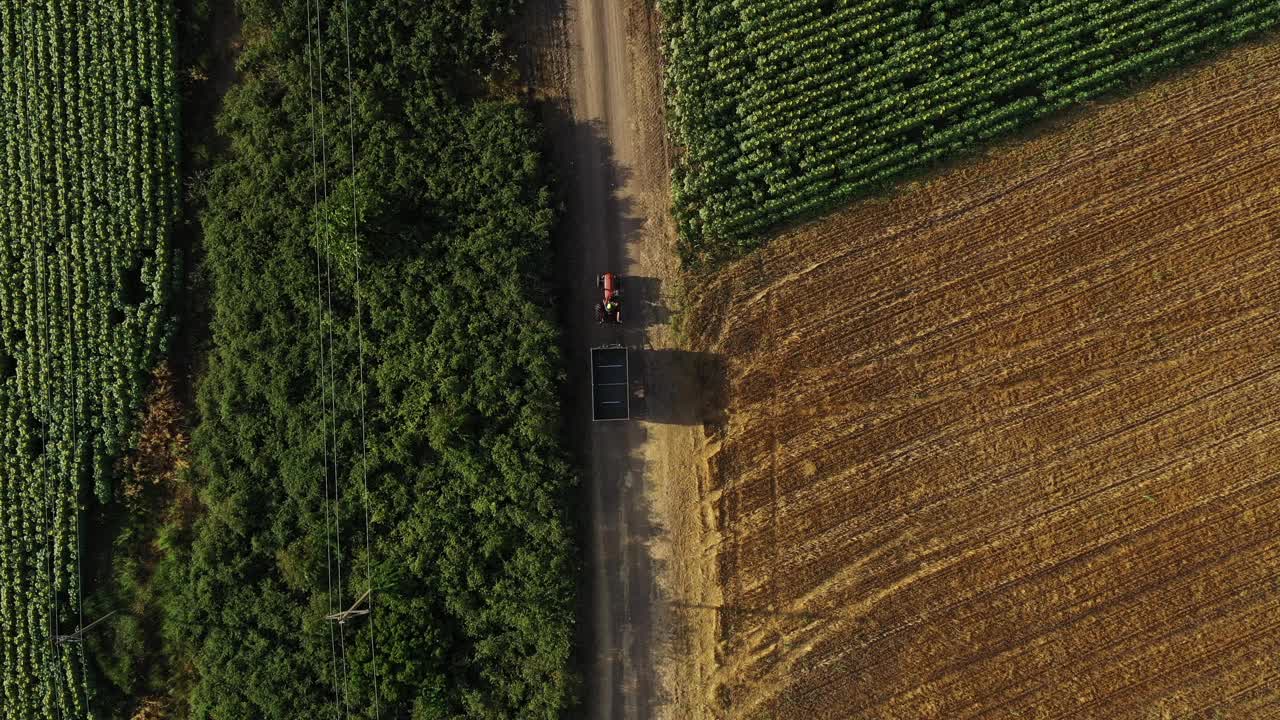 夏日里，农用拖拉机拖着空货车行驶在乡间的土路上，在地上投下阴影，无人机拍摄的航拍画面视频素材