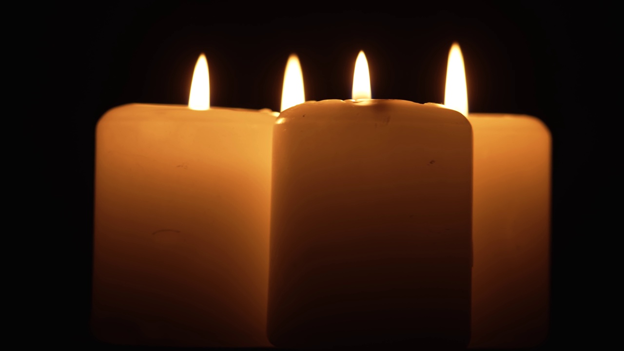 四根黄色的大蜡烛火焰在黑暗的背景上燃烧旋转视频下载