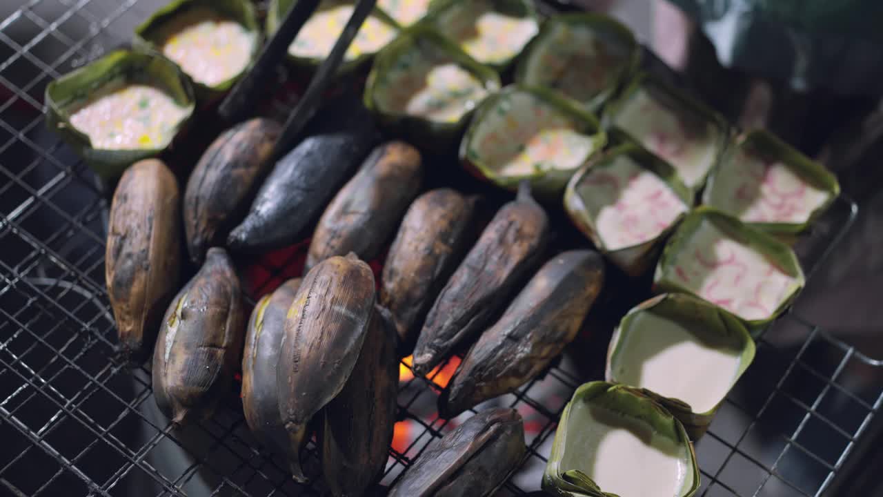 在街头食品市场的市场摊位上，香蕉和传统的泰国甜点放入香蕉叶，在金属格栅上烧烤，美味的泰国当地即食甜点视频素材
