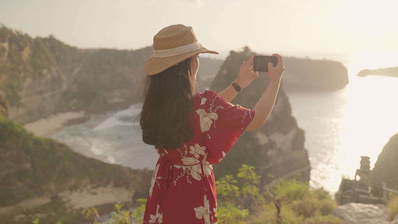 一名年轻的女游客站在观景台的4K视频，用手机拍摄努沙佩尼达岛的阿顿海滩和日出。印尼巴厘岛的热门旅游目的地。视频素材