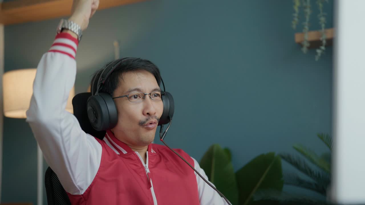 亚洲男子英俊的职业玩家戴着耳机玩在线视频游戏，在家里有直播。视频素材