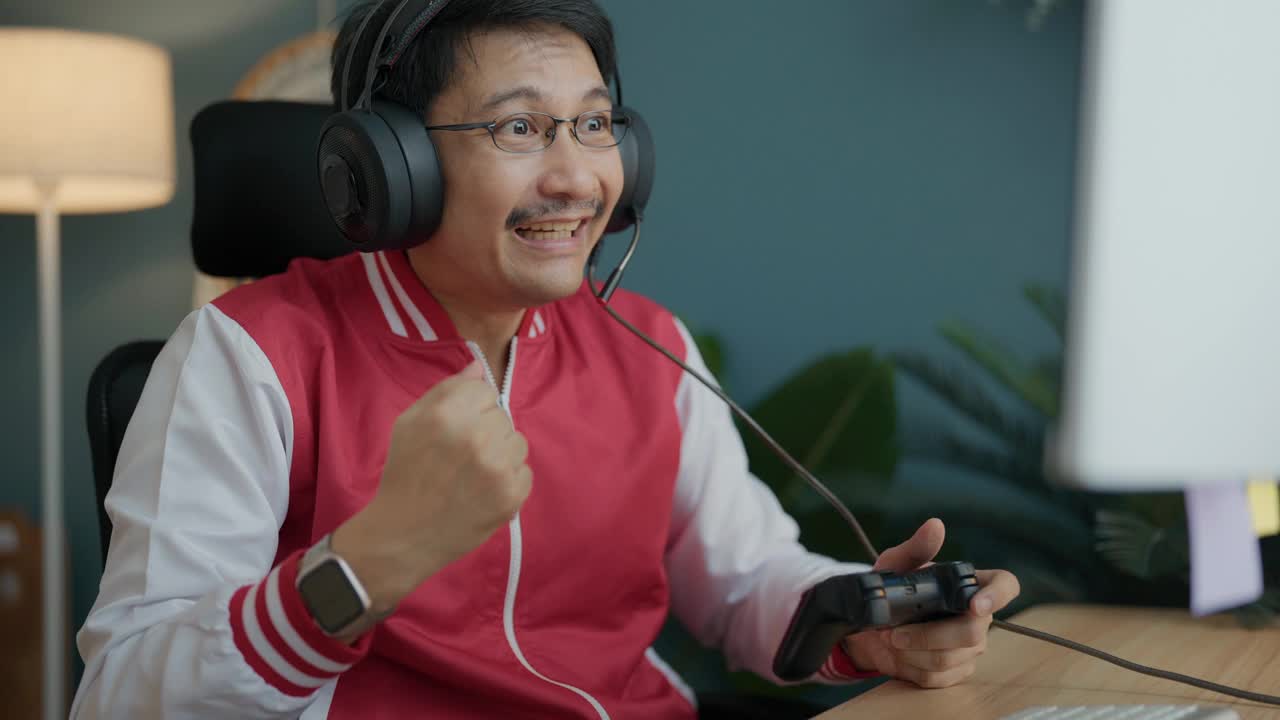 亚洲资深男性电子竞技玩家在房间里玩令人兴奋的在线游戏，他赢了，举起拳头，举起手臂。视频素材