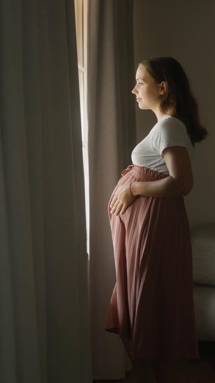孕妇在家里拉开窗帘望向窗外-垂直视频下载