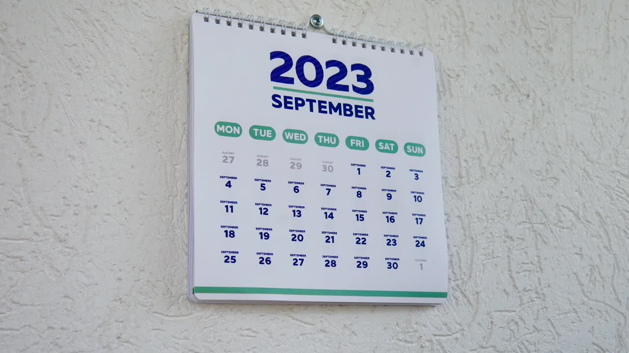 放大画面，两只男性的手撕掉了墙上的日历，2023年9月的那一页，紧接着是下一页，上面写着万圣节的日期视频素材