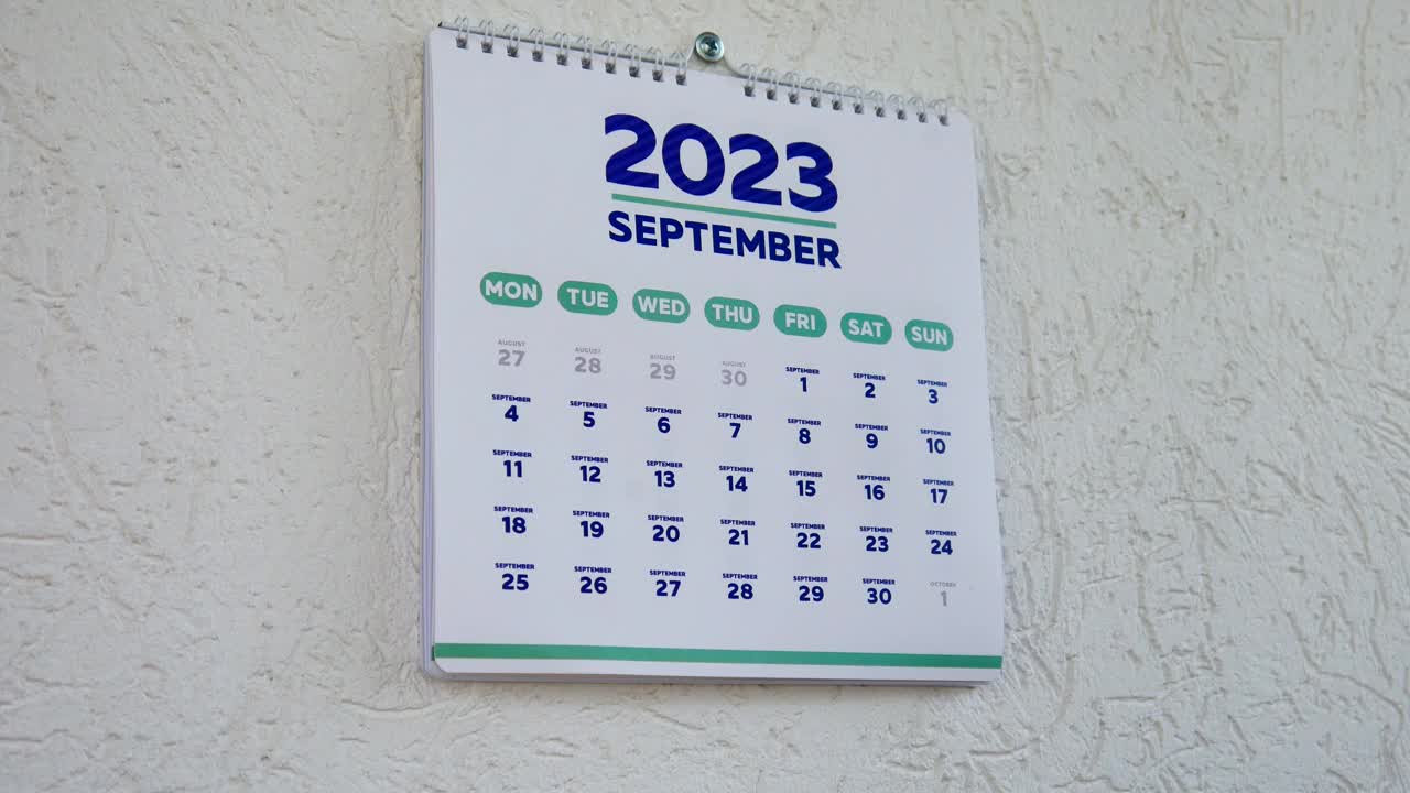 特写:两只男性的手撕掉了墙上的日历，2023年9月的那一页，紧接着是下一页，上面写着万圣节的日期视频素材