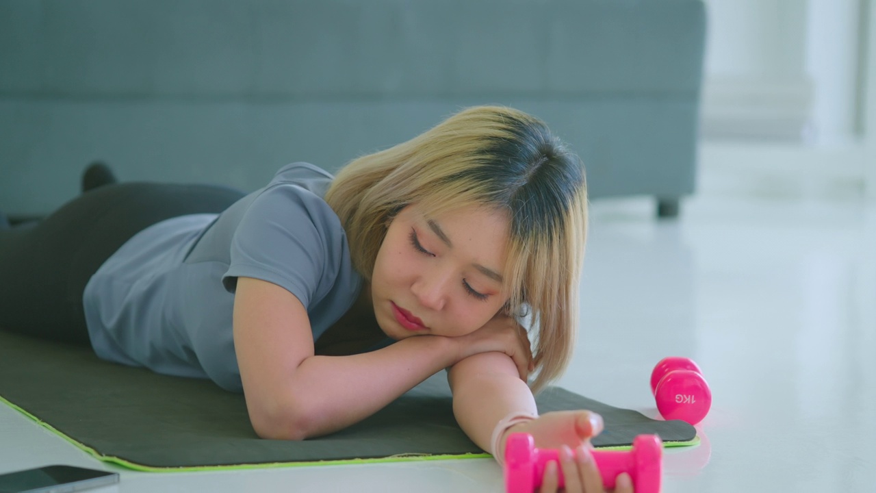 年轻的亚洲女性在尝试锻炼的时候与无聊和懒惰作斗争。视频下载