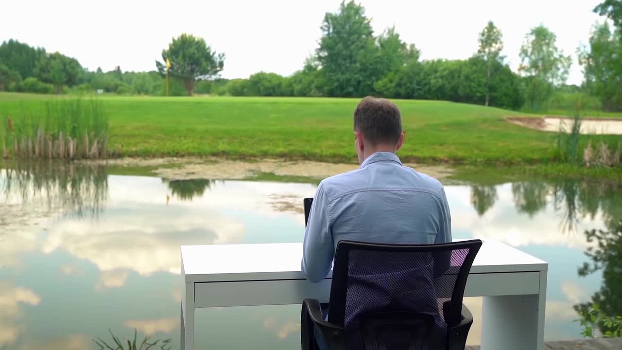 一名男子在河边的大自然办公桌旁工作视频下载