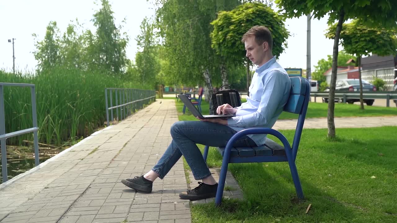 一名男子坐在海边的长凳上用笔记本电脑工作视频下载