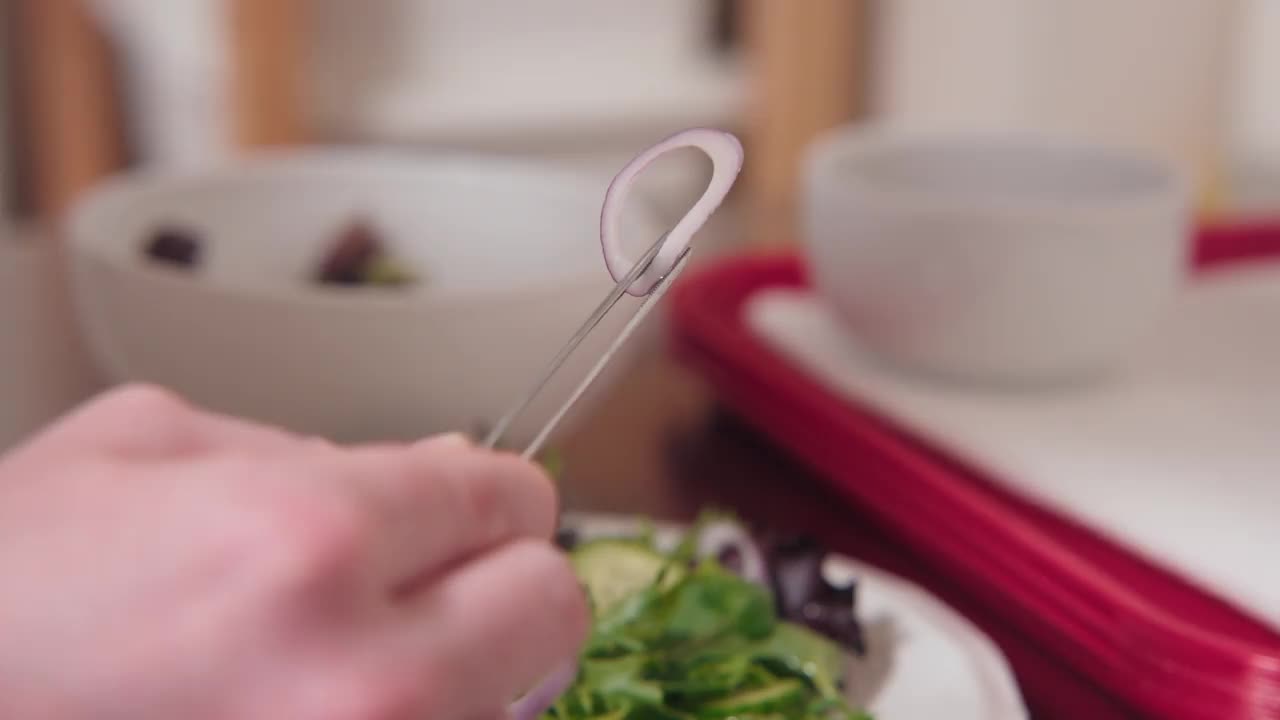 一位专业厨师美食摄影师烹饪艺术家将薄葱片放在绿叶沙拉碗上，在厨房工作空间中使用一套精致的镊子拍摄食物照片视频下载