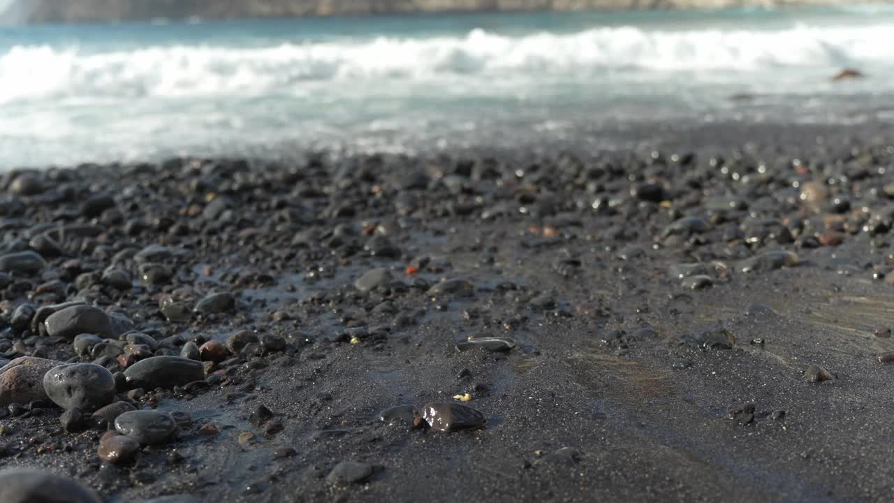 在特内里费岛的洛斯吉甘蒂斯，靠近火山沙子和鹅卵石，可以看到海浪和悬崖。视频下载
