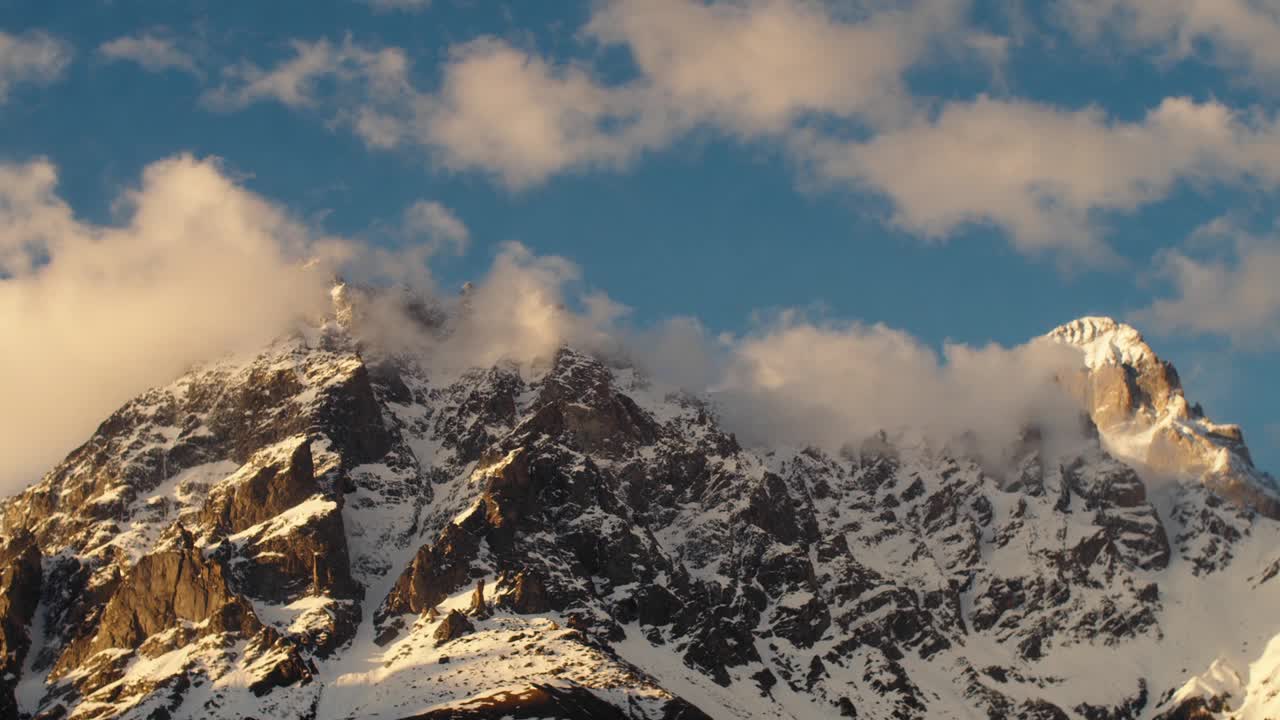 雪山覆盖着云延时视频。在一个阳光明媚的日子里，日落时美丽的山景。旅游目的地视频下载