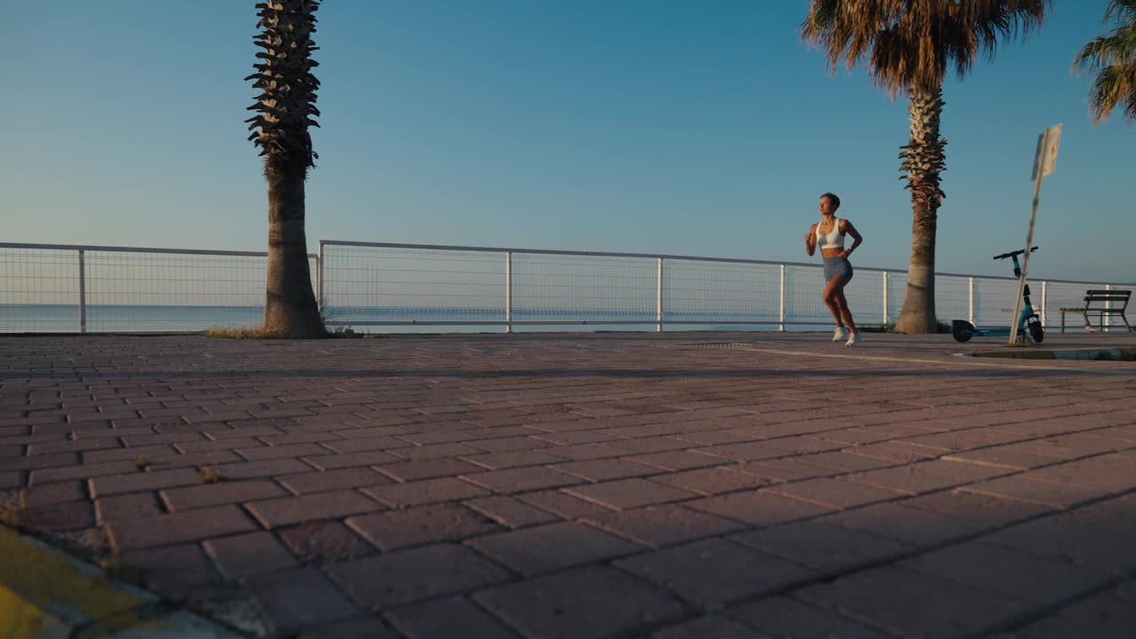 女子运动员在日落海滩慢跑。健身跑者女孩在海边训练，在美丽的日落或日出在夏天全身长度。缓慢的运动。高品质4k画面视频素材