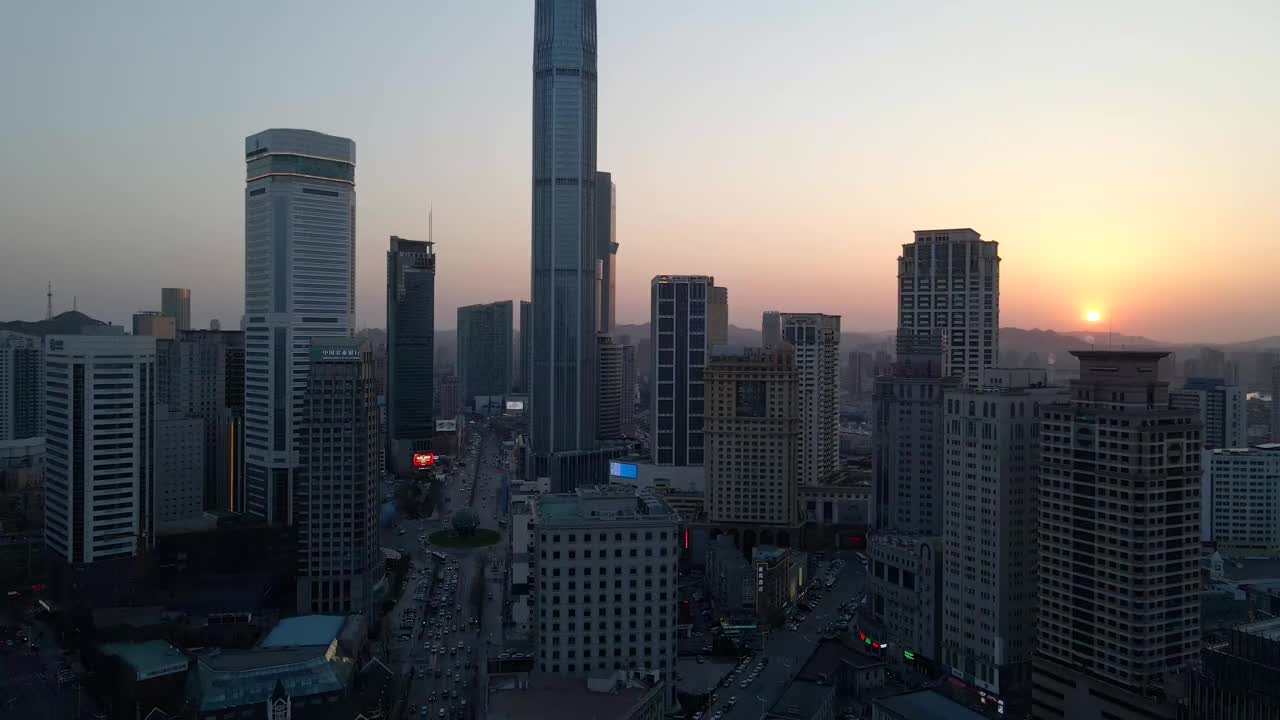 航拍无人机在日落时分盘旋在中山广场上，俯瞰大连的摩天大楼视频下载