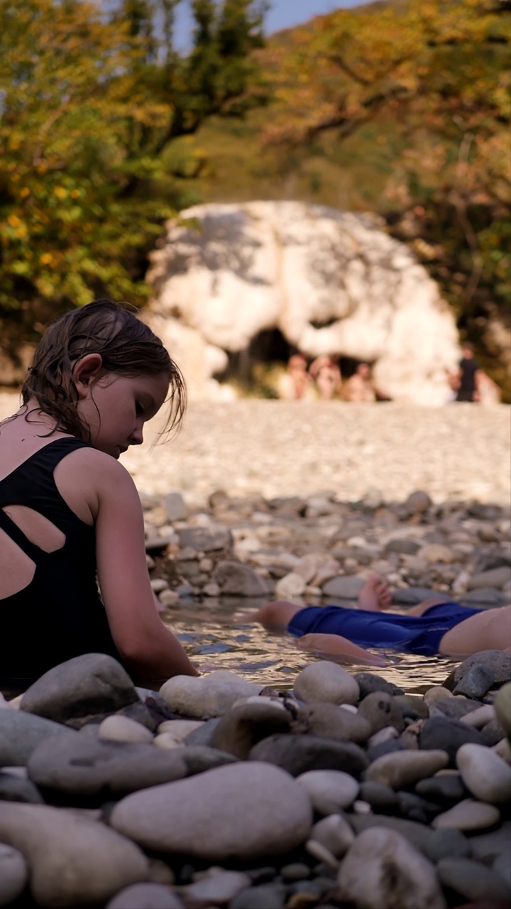 两个姐妹正在一个小地热泉里洗澡，温泉的岸边是由圆形光滑的石头组成的岩石。在温暖的温泉中享受天然水疗。垂直视频视频下载