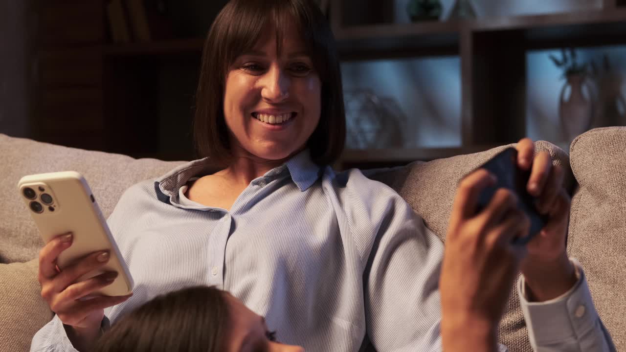 母亲和儿子晚上在沙发上玩手机视频下载