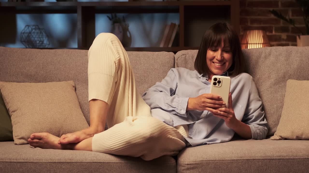 微笑的白人妇女晚上在沙发上使用电话视频素材