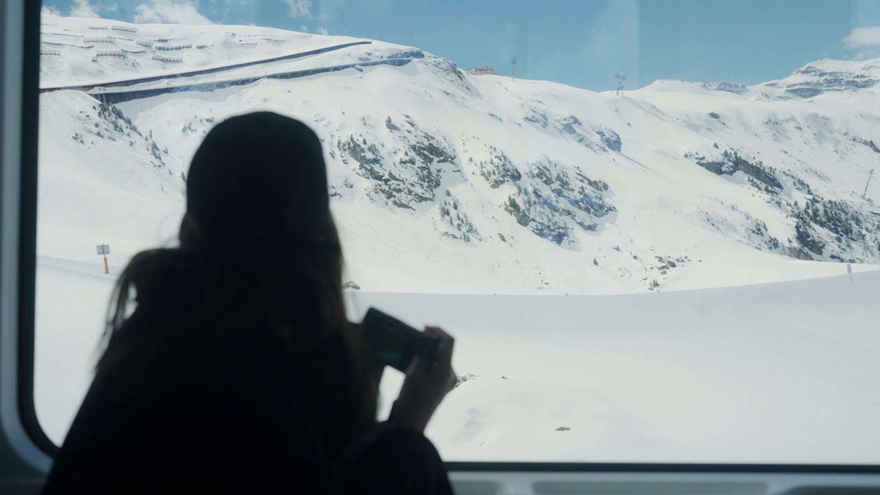 一名亚洲女游客在瑞士雪山上的火车上拍摄度假照片。视频下载