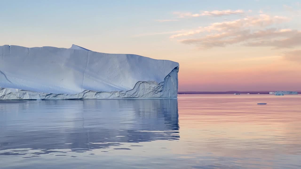 北维斯特峡湾日落后巨大的冰山飘过。美丽的倒影。Scoresbysund,格陵兰岛。视频下载