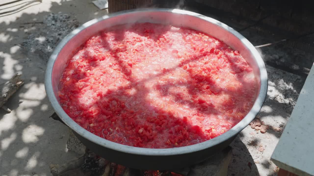在阳光明媚的日子里，在户外的篝火上制作番茄酱:切成丁的西红柿在锅里用火煨着，非常适合做披萨或罐头。视频下载