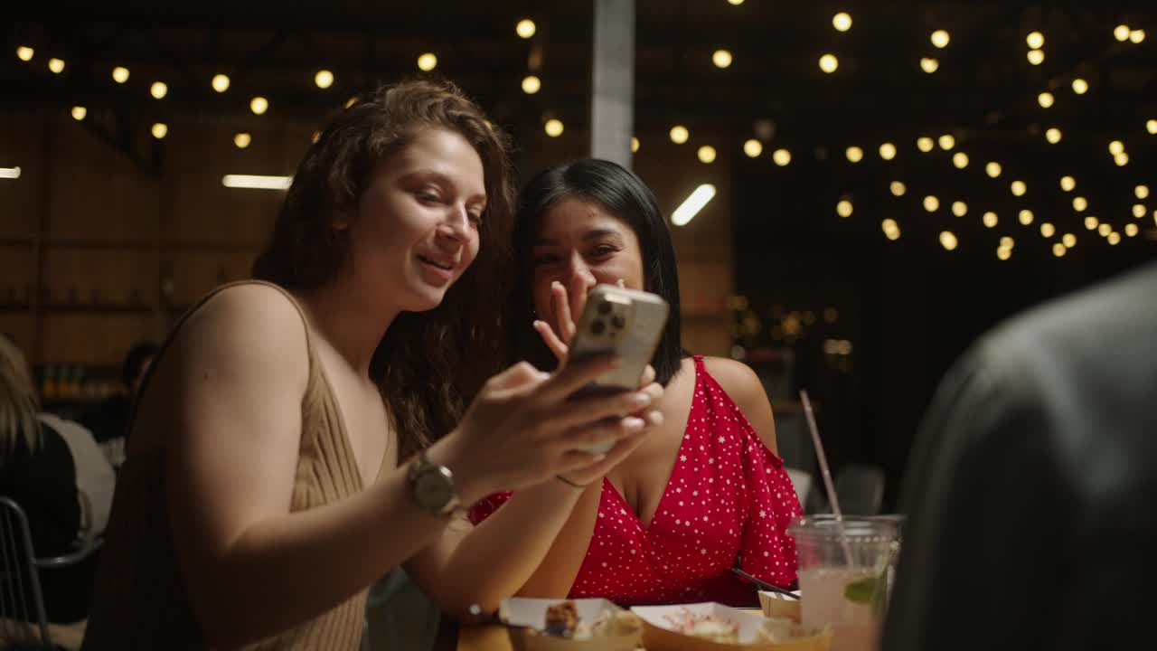 多民族女性朋友在智能手机上看照片，在餐厅吃饭视频下载