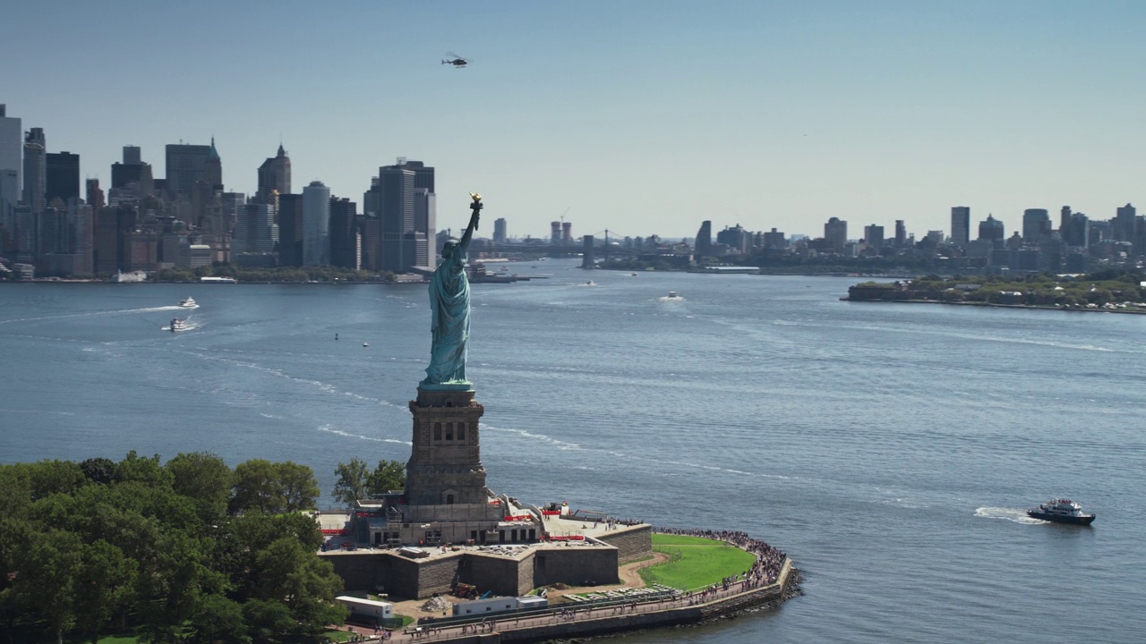 空中直升机的电影通过视图的自由女神像与曼哈顿天际线城市景观。在一个阳光明媚的日子里，纽约市摩天大楼和泽西城建筑的全景视频下载