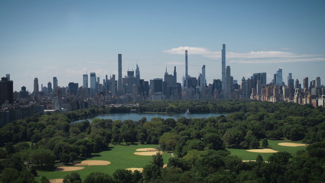 空中直升机镜头在中央公园与自然，树木，人们野餐和休息在曼哈顿摩天大楼周围的田野景观。美丽的晴天。慢动作镜头视频下载