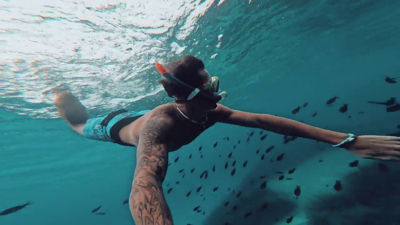 一个年轻的漂亮的活跃的男人游泳和享受户外假期在海上浮潜寻找鱼和珊瑚。男性旅行者拿着相机在蓝色的海洋里玩得很开心视频素材
