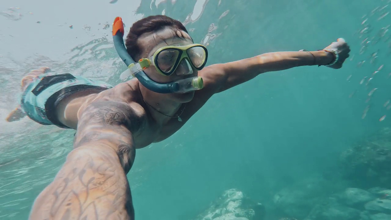 一个年轻的漂亮的活跃的男人游泳和享受户外假期在海上浮潜寻找鱼和珊瑚。男性旅行者拿着相机在蓝色的海洋里玩得很开心视频下载