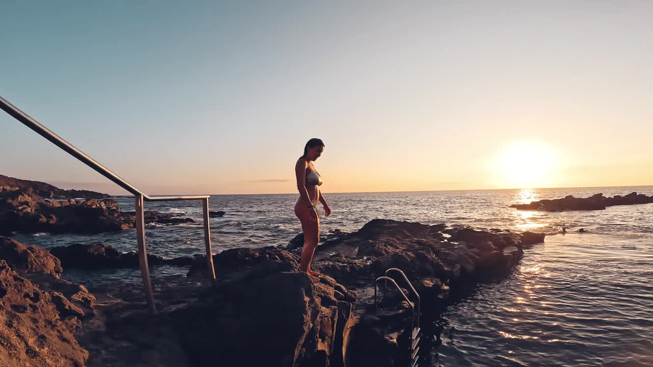 一个年轻快乐迷人的女孩在蓝色的海洋里奔跑和跳跃，享受和享受假期的乐趣，无忧无虑的概念生活方式。沙滩上的美女。视频下载
