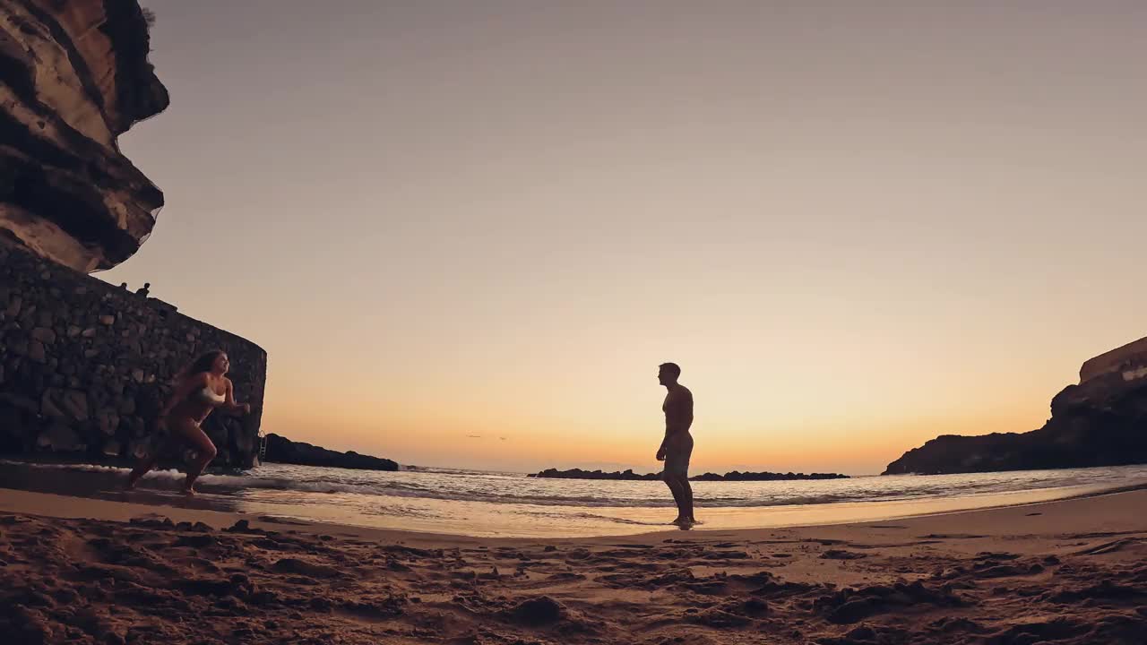 一个快乐可爱的女人在日落的沙滩上奔向她的男友。幸福的千禧一代情侣一起享受。年轻男子抱着女友视频下载