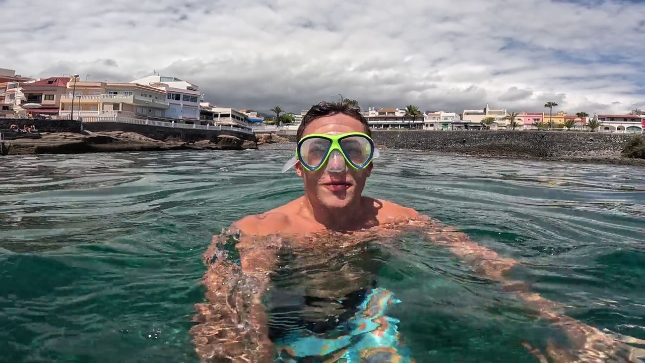 一个年轻的漂亮的活跃的男人游泳和享受户外假期在海上浮潜寻找鱼和珊瑚。男性旅行者拿着相机在蓝色的海洋里玩得很开心视频下载
