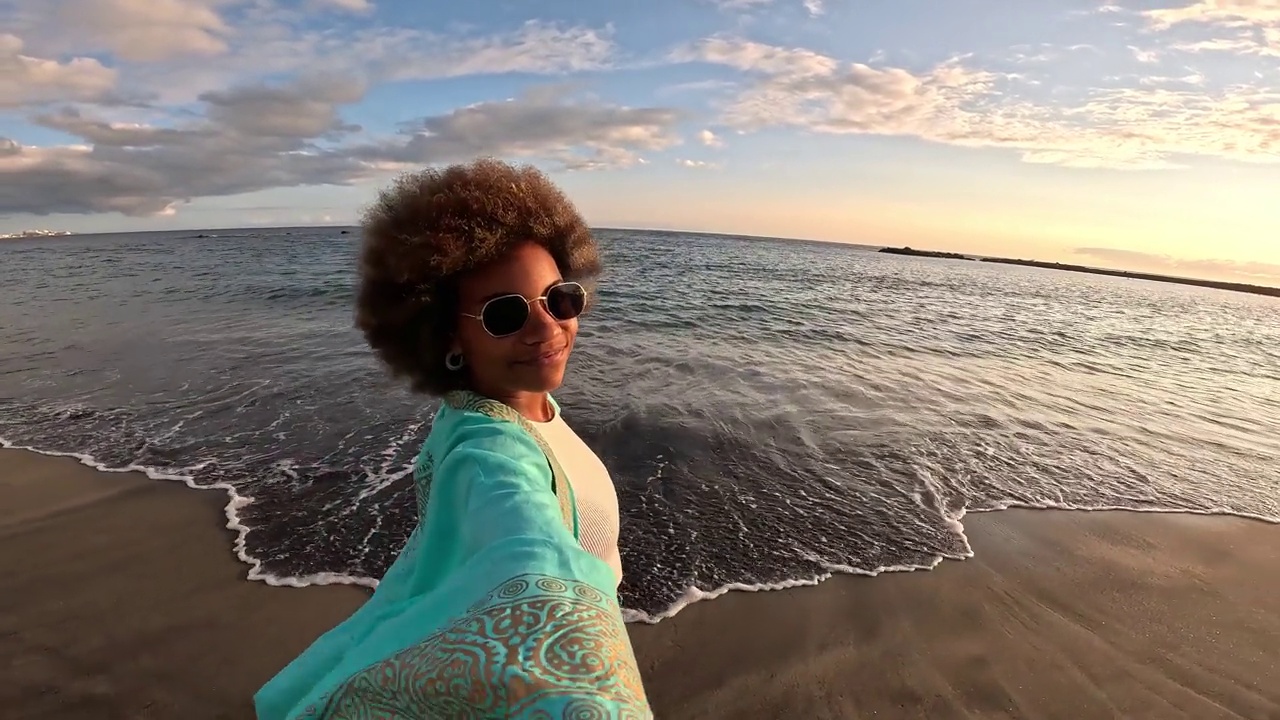 一个非洲多种族的年轻美女拿着相机在海滩上自拍，享受夏日户外度假。视频素材