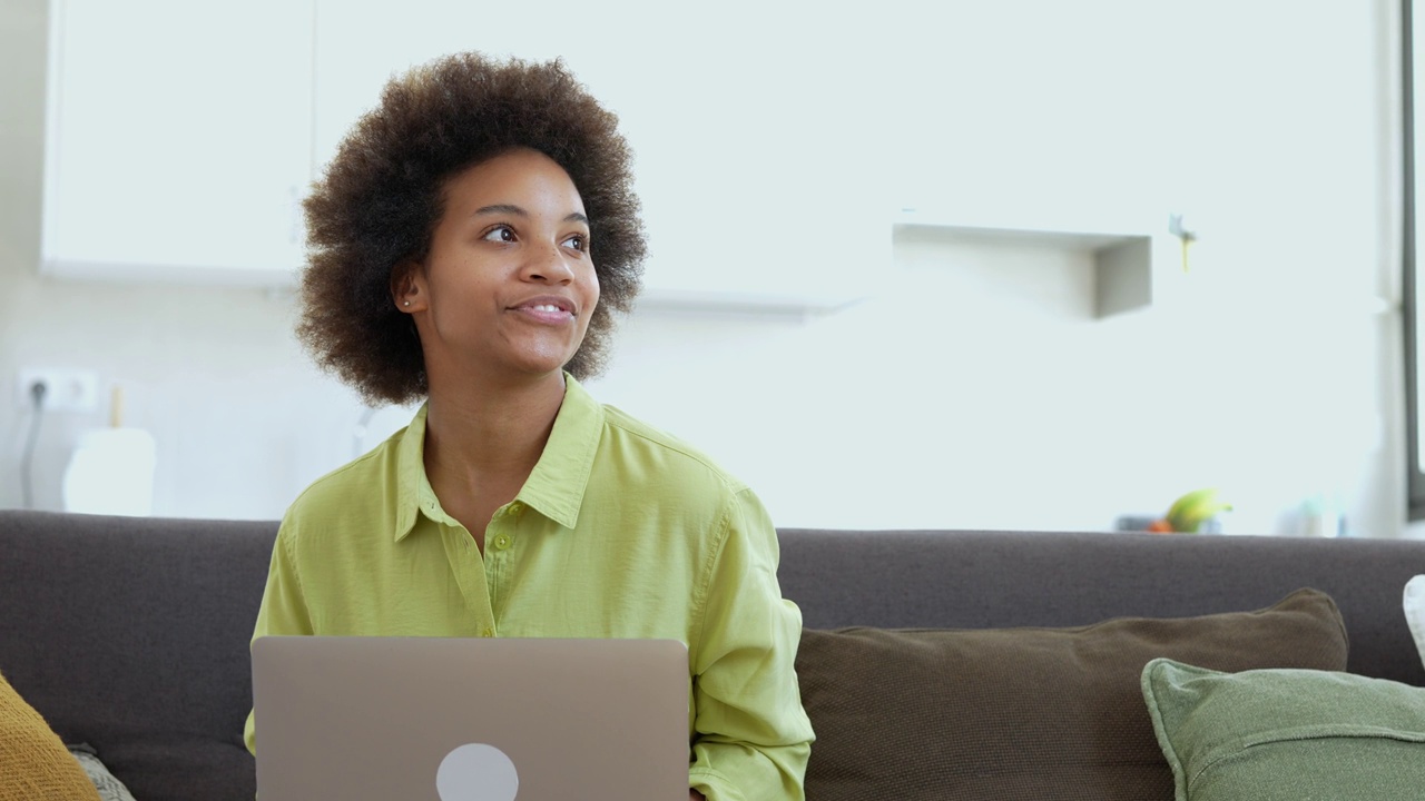 容易学习。微笑的年轻混血女士坐在沙发上，用笔记本电脑搜索信息，观看网络研讨会视频课程。积极的黑人女性利用在线教育服务提高挥动技能视频素材