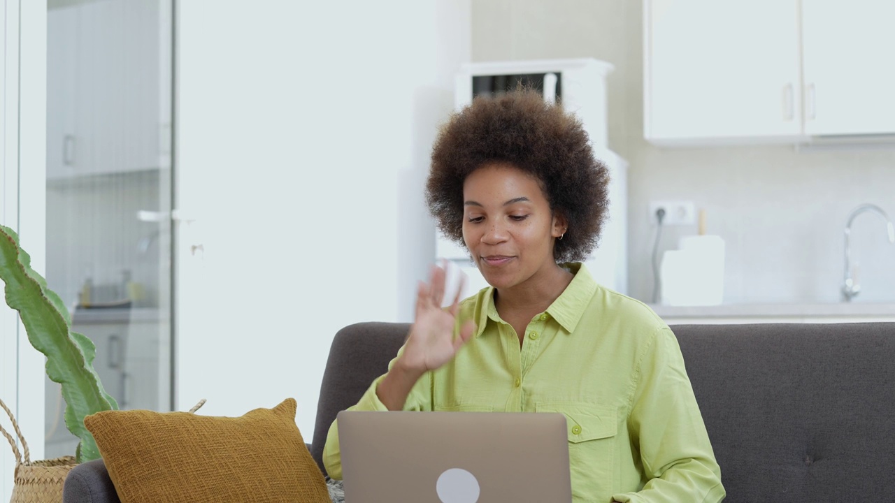 容易学习。微笑的年轻混血女士坐在沙发上，用笔记本电脑搜索信息，观看网络研讨会视频课程。积极的黑人女性利用在线教育服务提高挥动技能视频下载