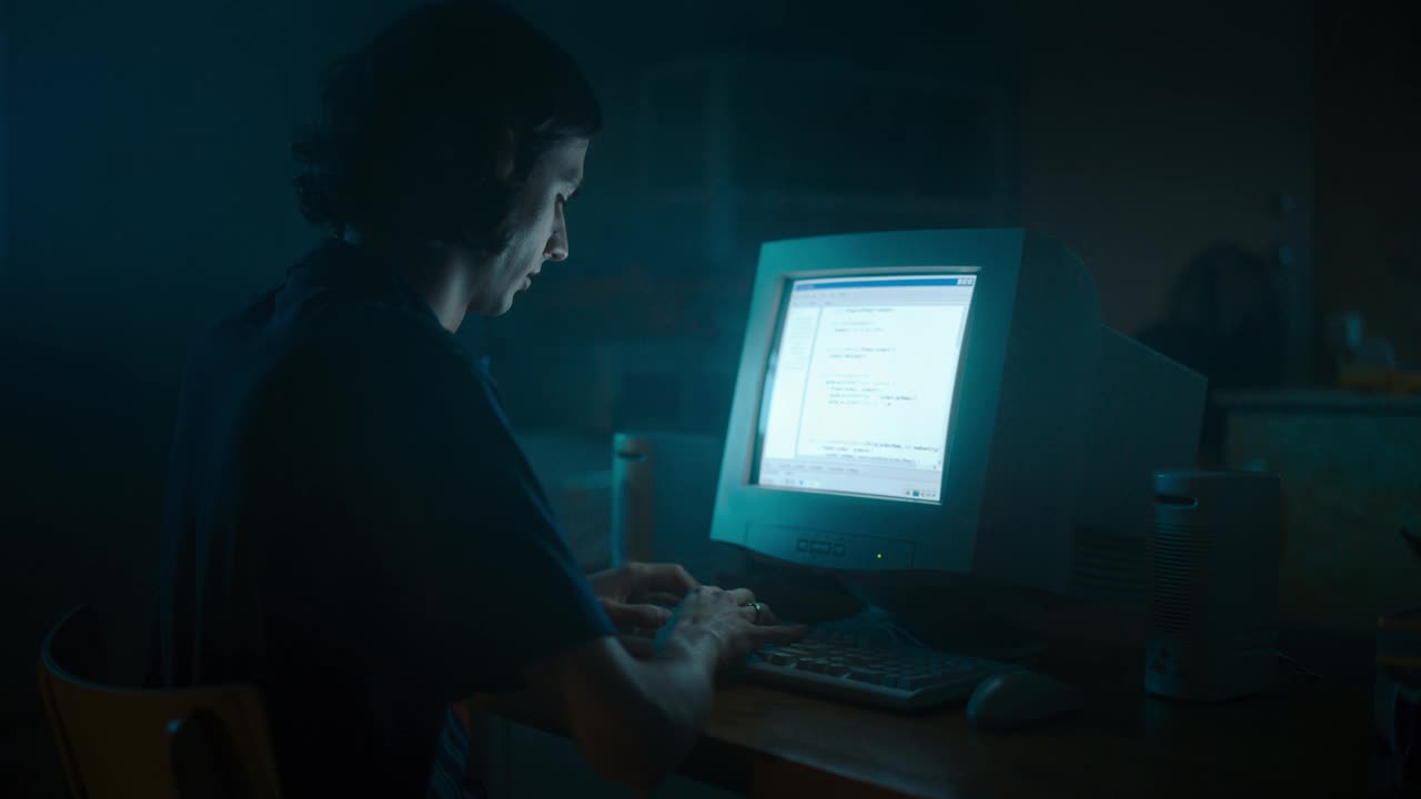 白人男性网页设计师深夜在复古车库使用旧台式电脑。专注的互联网爱好者在家写代码。九十年代成功的社交网站编程。视频素材