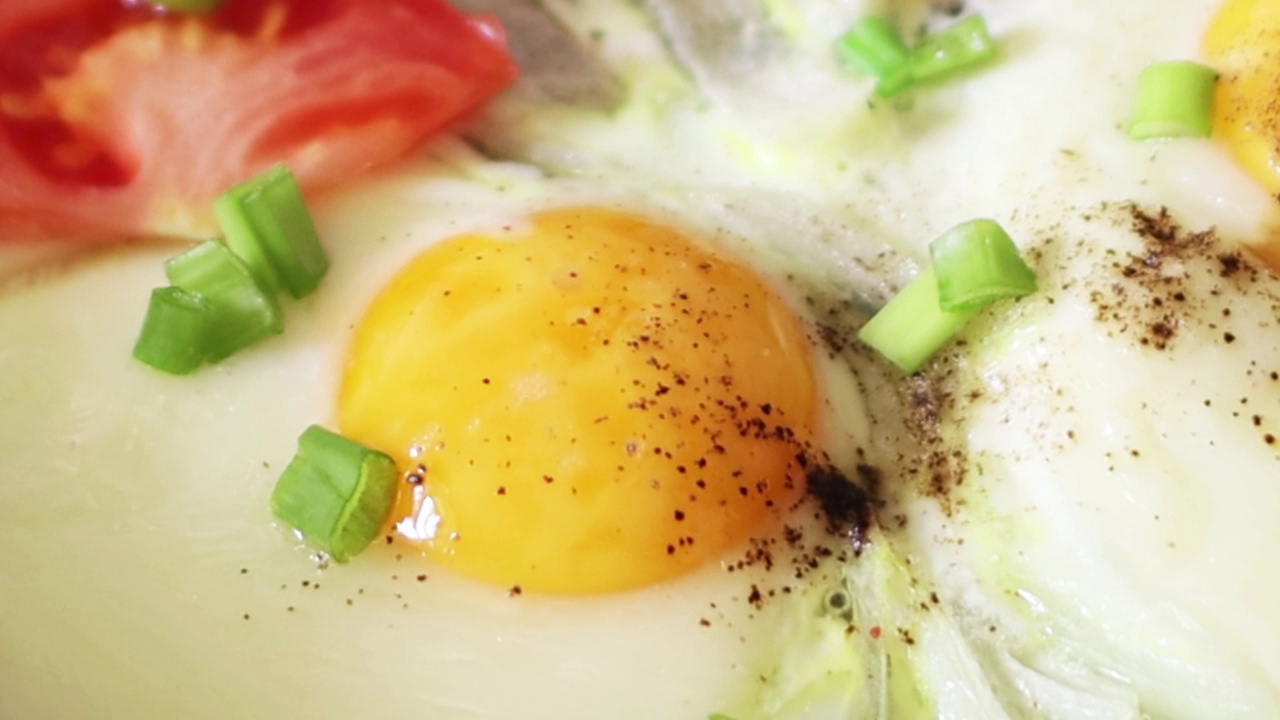 煎鸡蛋，用葱、西红柿、香料在锅里煎。早餐。特写镜头。4 k的决议视频下载