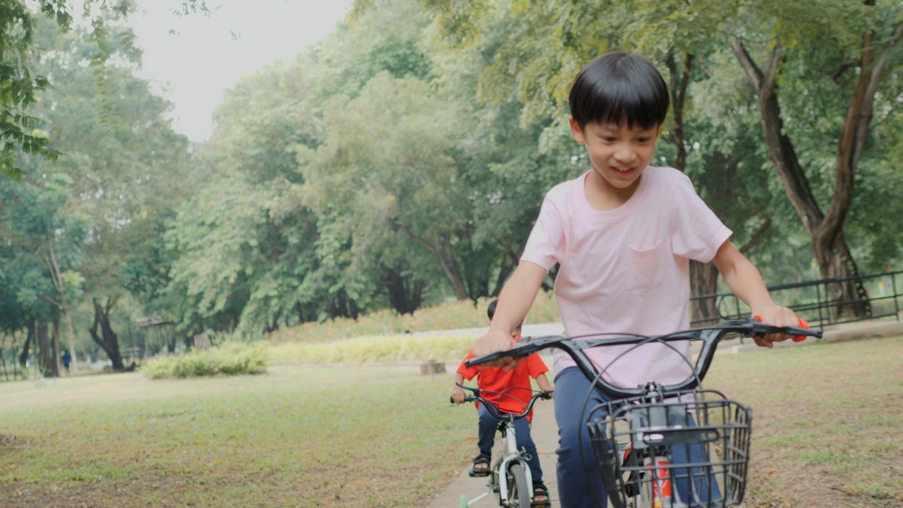 两个亚洲男孩在公园里愉快地骑着自行车。视频下载