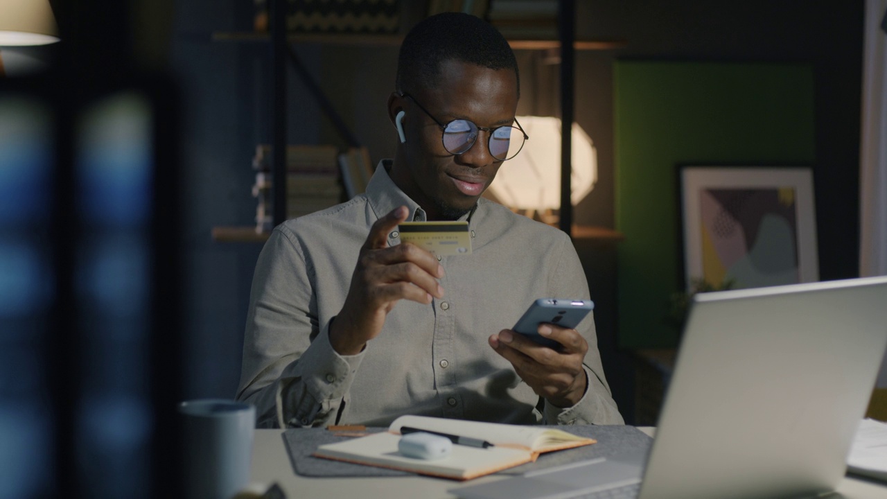 非洲裔美国商人在漆黑的办公室里用智能手机和信用卡付款视频素材