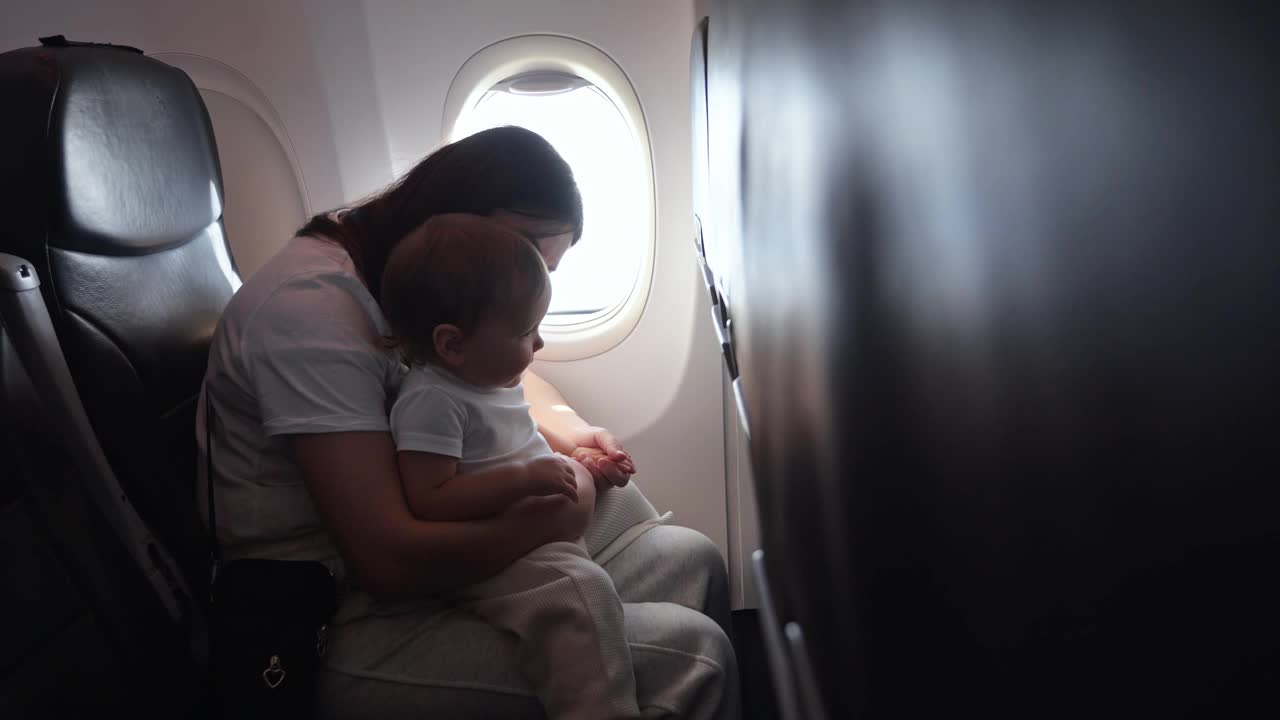 慈祥的妈妈在飞机上爱抚着蹒跚学步的小女孩视频下载