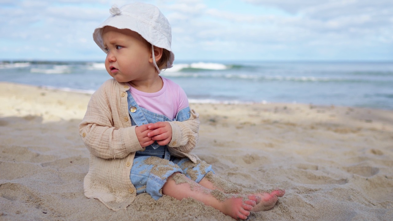 小女孩坐在海边的沙滩上，把脚埋在沙子里视频下载