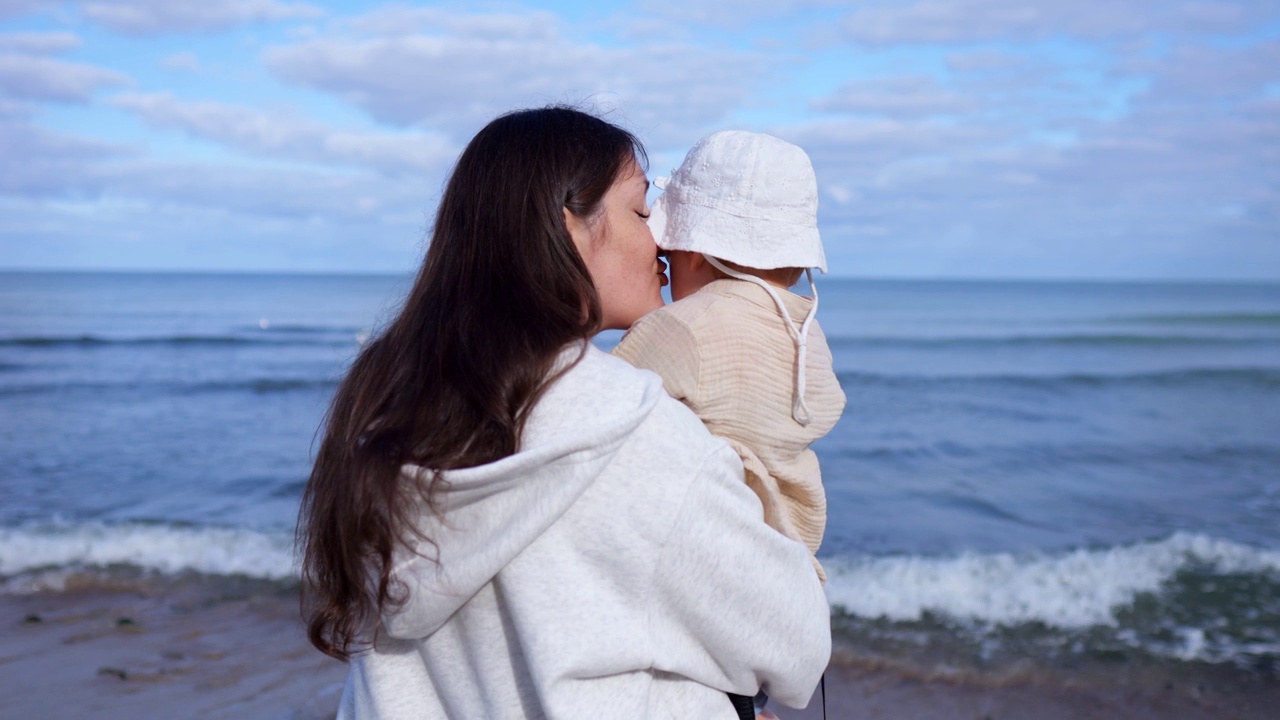 妈妈小心地把女儿抱在怀里，看着海浪视频下载