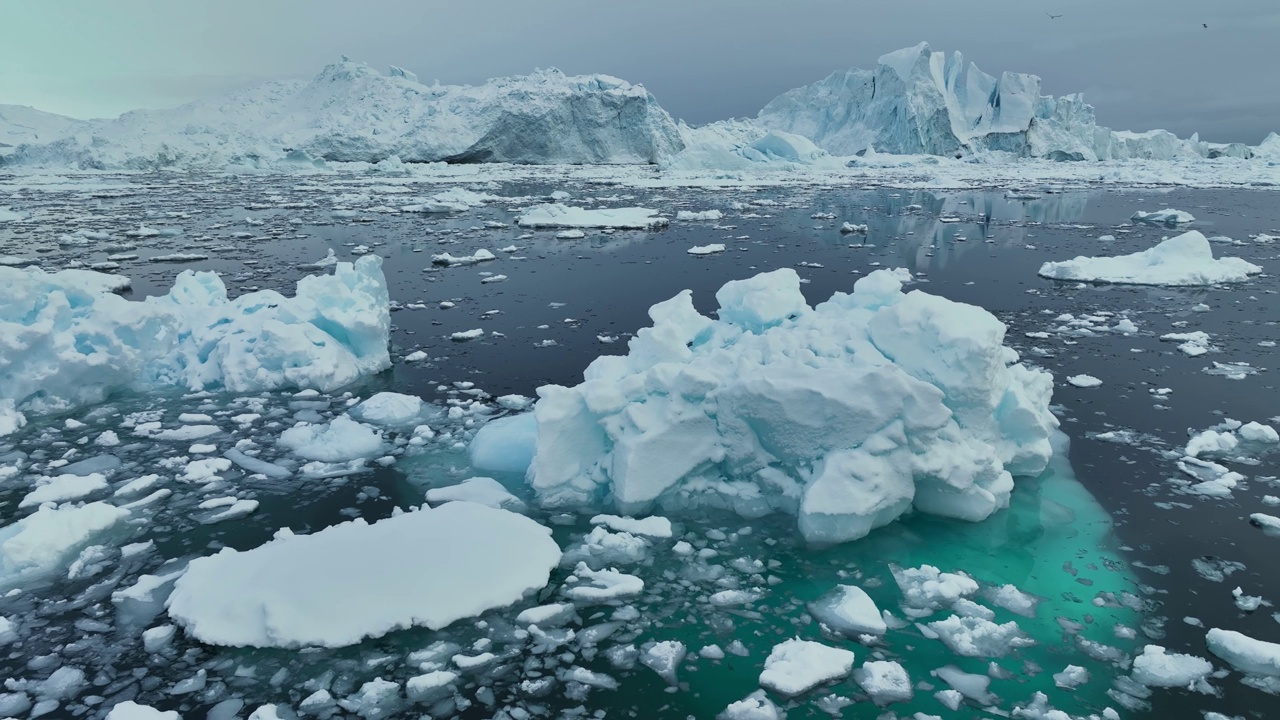 飞越格陵兰岛伊卢利萨特附近的巨大冰山。海洋中被雪覆盖的巨大冰山。空中北极自然景观，全球变暖和气候变化的概念视频下载