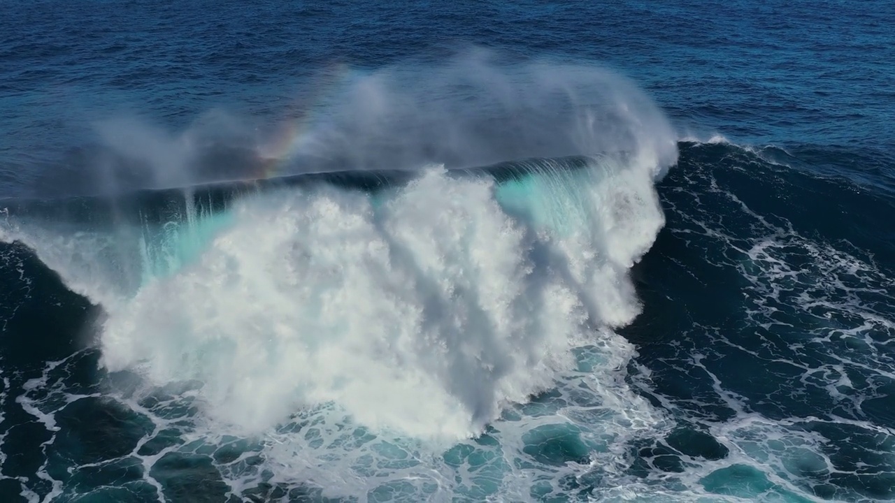 巨大的海浪带着蓝绿色的水冲出海岸，形成水花和白色的泡沫。航拍强大的海浪与小彩虹。极端史诗般的飞行非常接近海洋的波浪表面视频下载