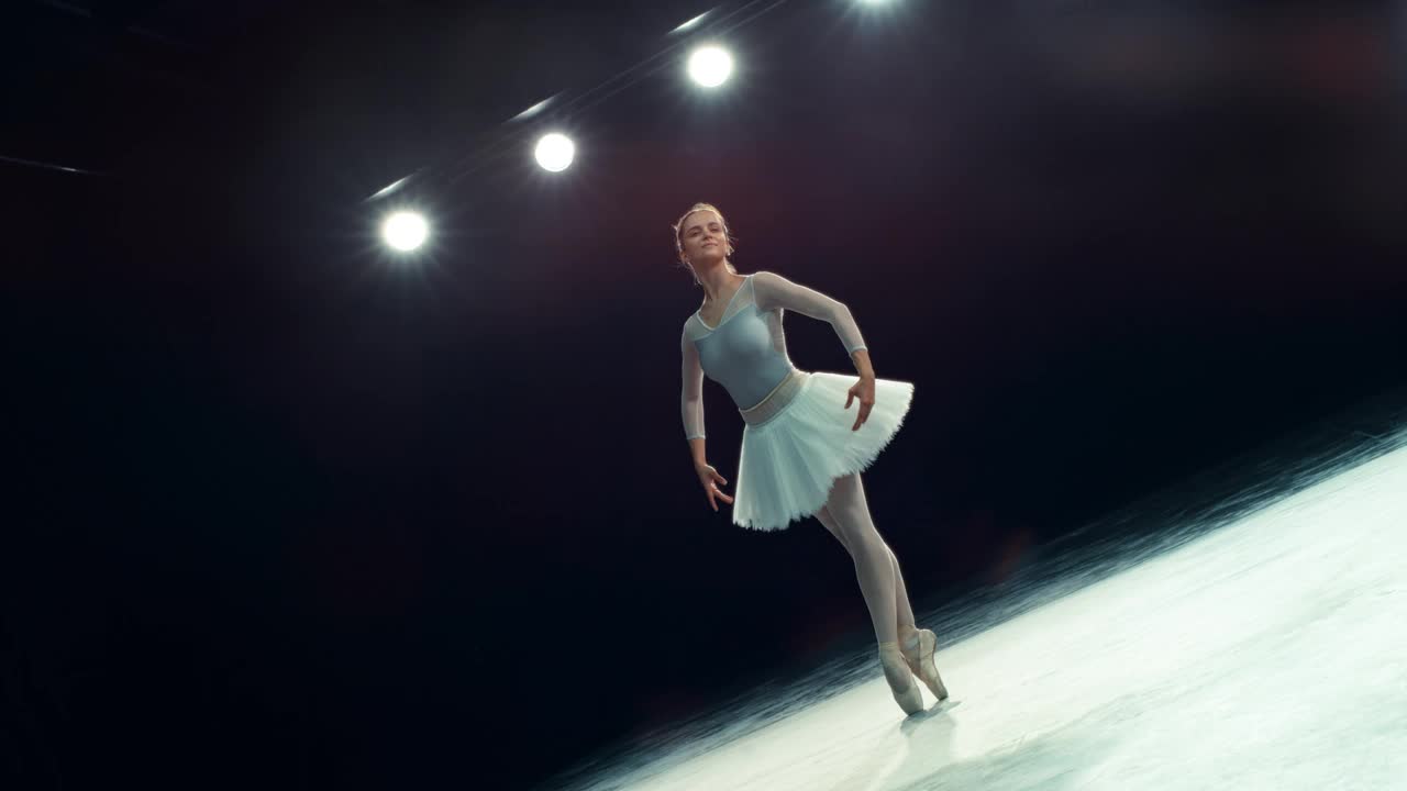 一位才华横溢的芭蕾舞女演员在有灯光的黑暗舞台上跳舞的电影表演。年轻的女性穿着漂亮的衣服，跳芭蕾舞，用脚趾旋转和跳跃视频素材