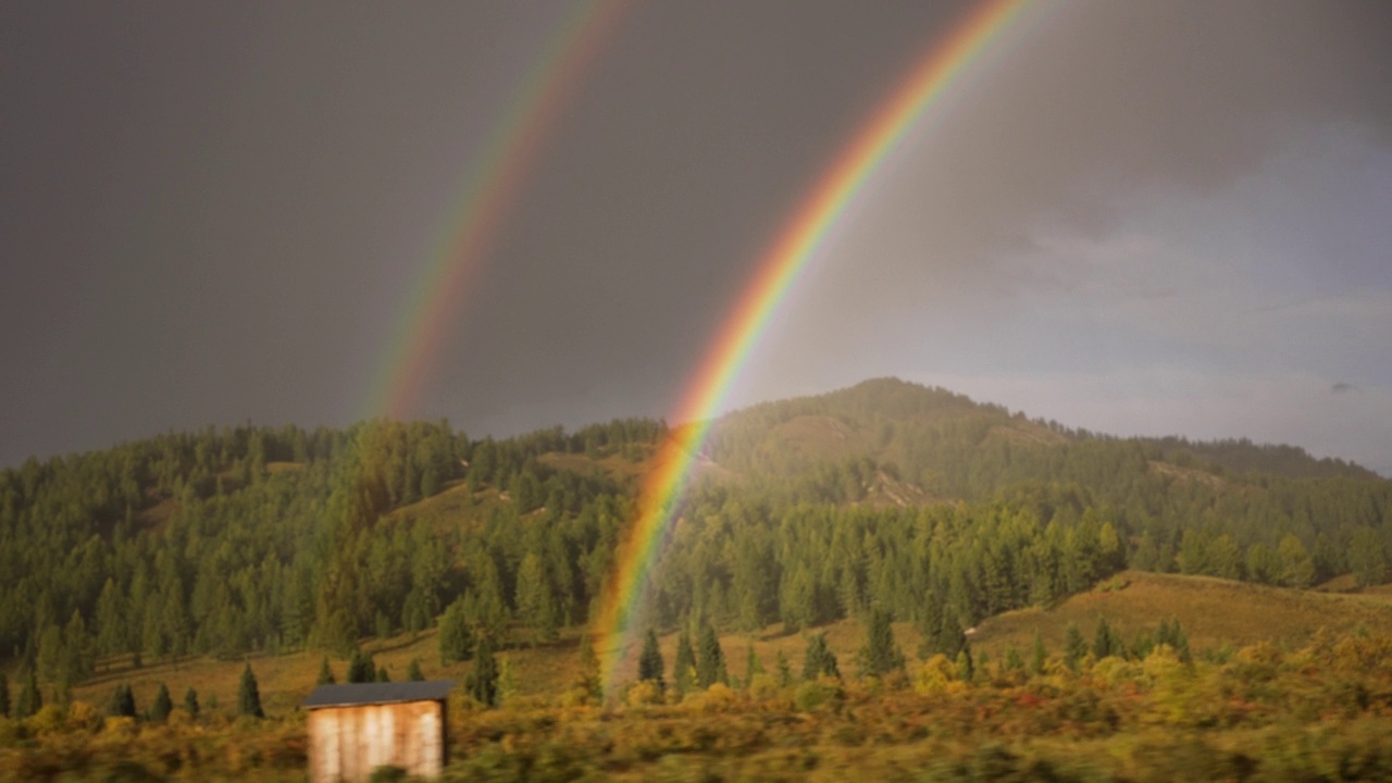 从车窗看到一道明亮美丽的彩虹，映衬着群山和针叶林视频下载