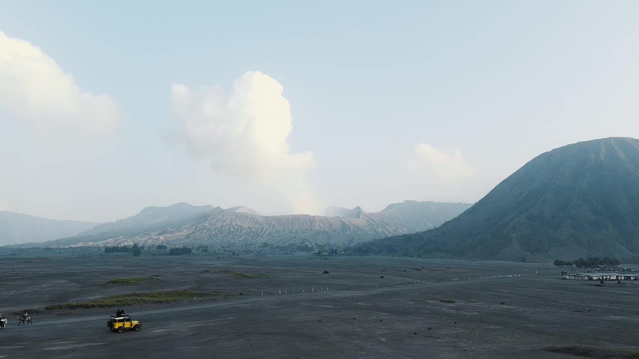 无人机拍摄的印尼布罗莫火山附近的沙漠，一辆吉普车骑在沙滩上。视频下载