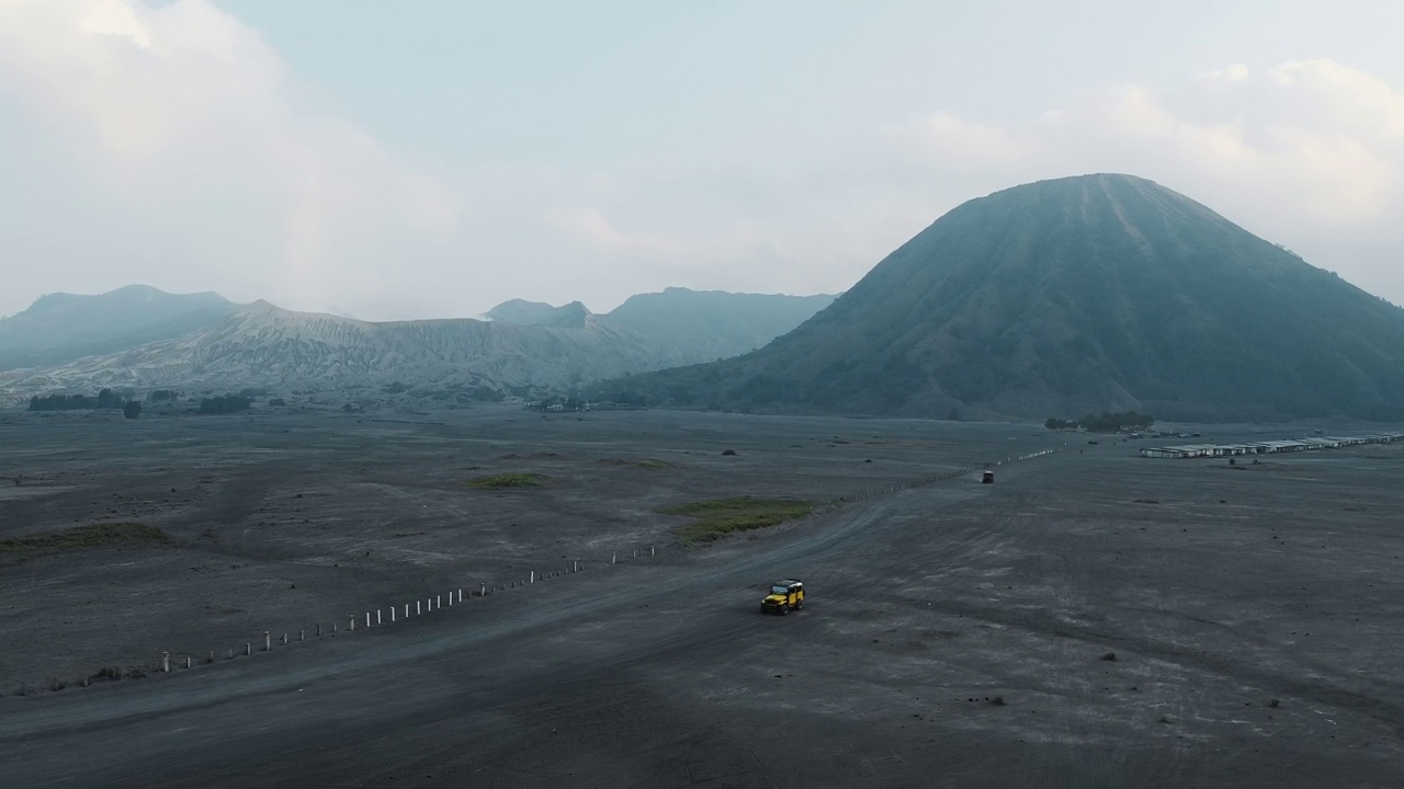 无人机拍摄的印尼布罗莫火山附近的沙漠，一辆吉普车骑在沙滩上。视频下载