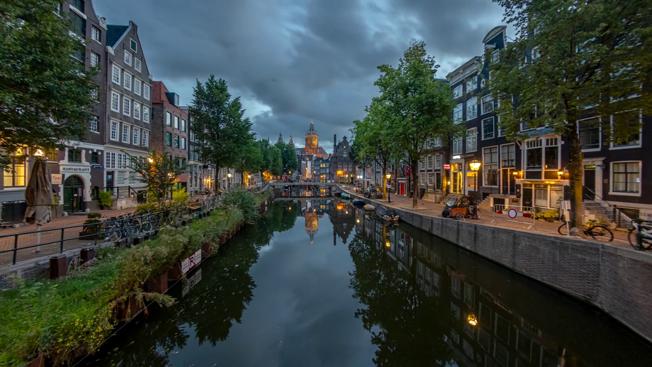 日出时，荷兰阿姆斯特丹一条典型的运河上的圣尼古拉斯大教堂从黑夜到白天的时间流逝视频下载