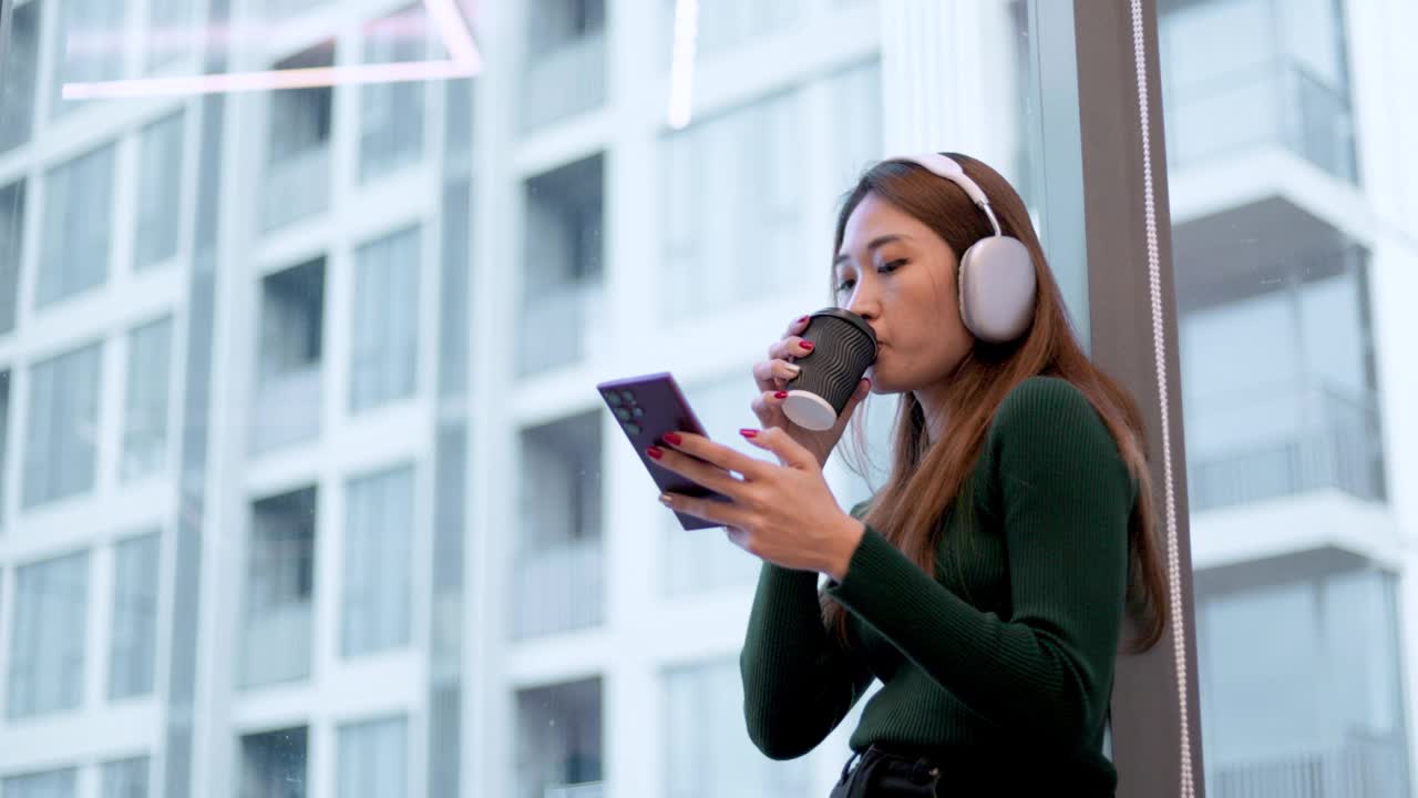 亚洲年轻女子在现代家庭靠窗边玩手机听音乐视频下载