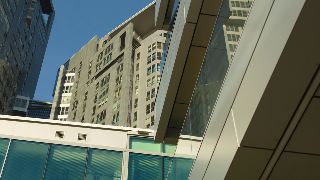 现代城市建筑有着光滑的玻璃外墙和高耸的公寓楼，映衬着晴朗的天空。视频素材
